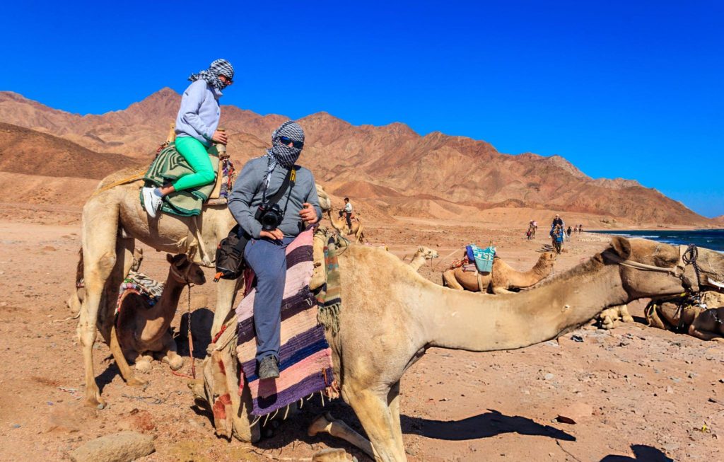 Tourist riding a camel through the rocky desert landscape during Dahab safari